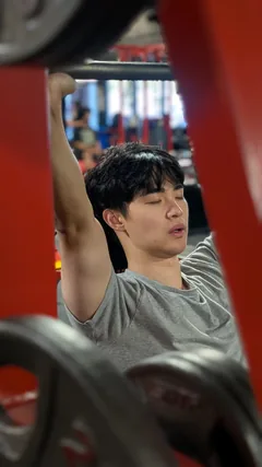 A man in a gray shirt using a shoulder-press machine.