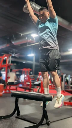 A man in a teal shirt hanging from an overhead exercise bar.