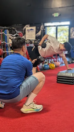 A trainer observing a client performing a plank row with a dumbbell.