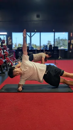 A man holding a side plank with one arm extended upward.