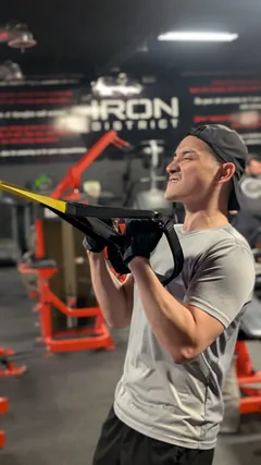 A smiling man pulling on suspension-training straps.