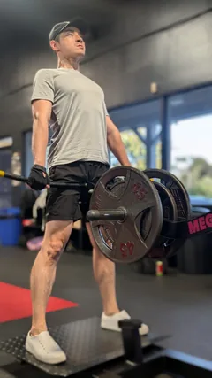A man in a gray shirt holding a loaded barbell at the top of a lift.