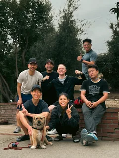 A group and two dogs gathered beside a brick wall outdoors.