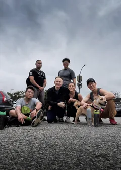 A hiking group with dogs gathered on a rocky summit under a cloudy sky.