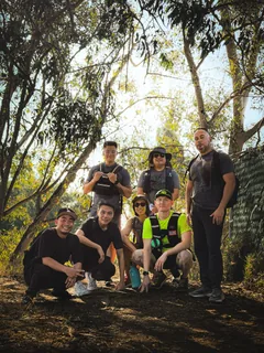 A hiking group gathered beneath trees beside a trail.