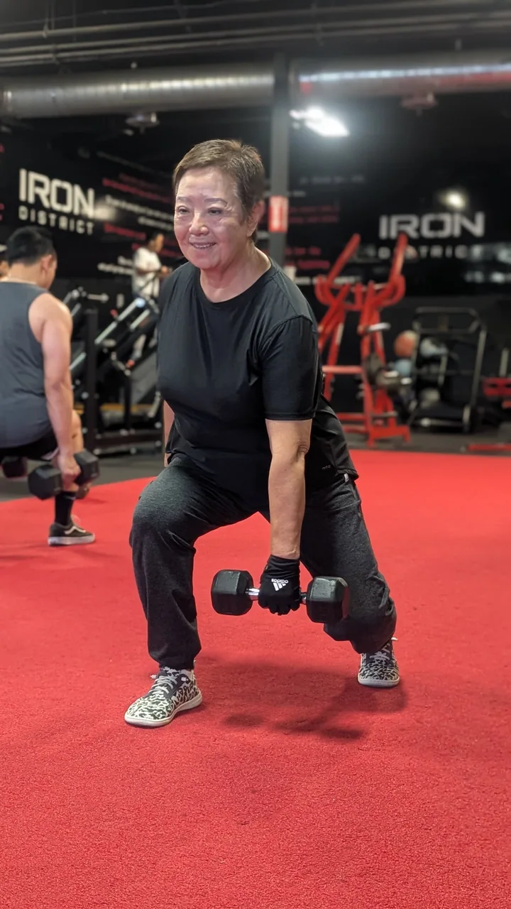 A smiling woman holding dumbbells in a split stance.