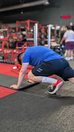 A man in a blue shirt performing a floor exercise on a mat.