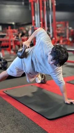 A man holding a plank beside a kettlebell on a mat.