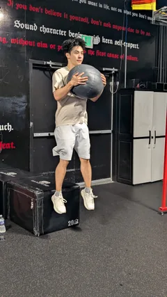 A man jumping while holding a medicine ball beside a box.
